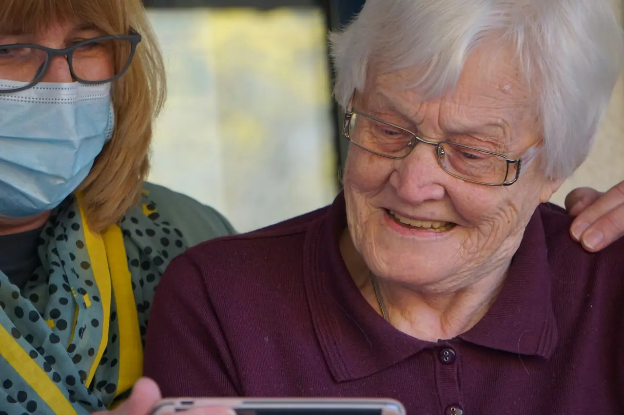 A carer and an older woman smiling together while looking at a phone