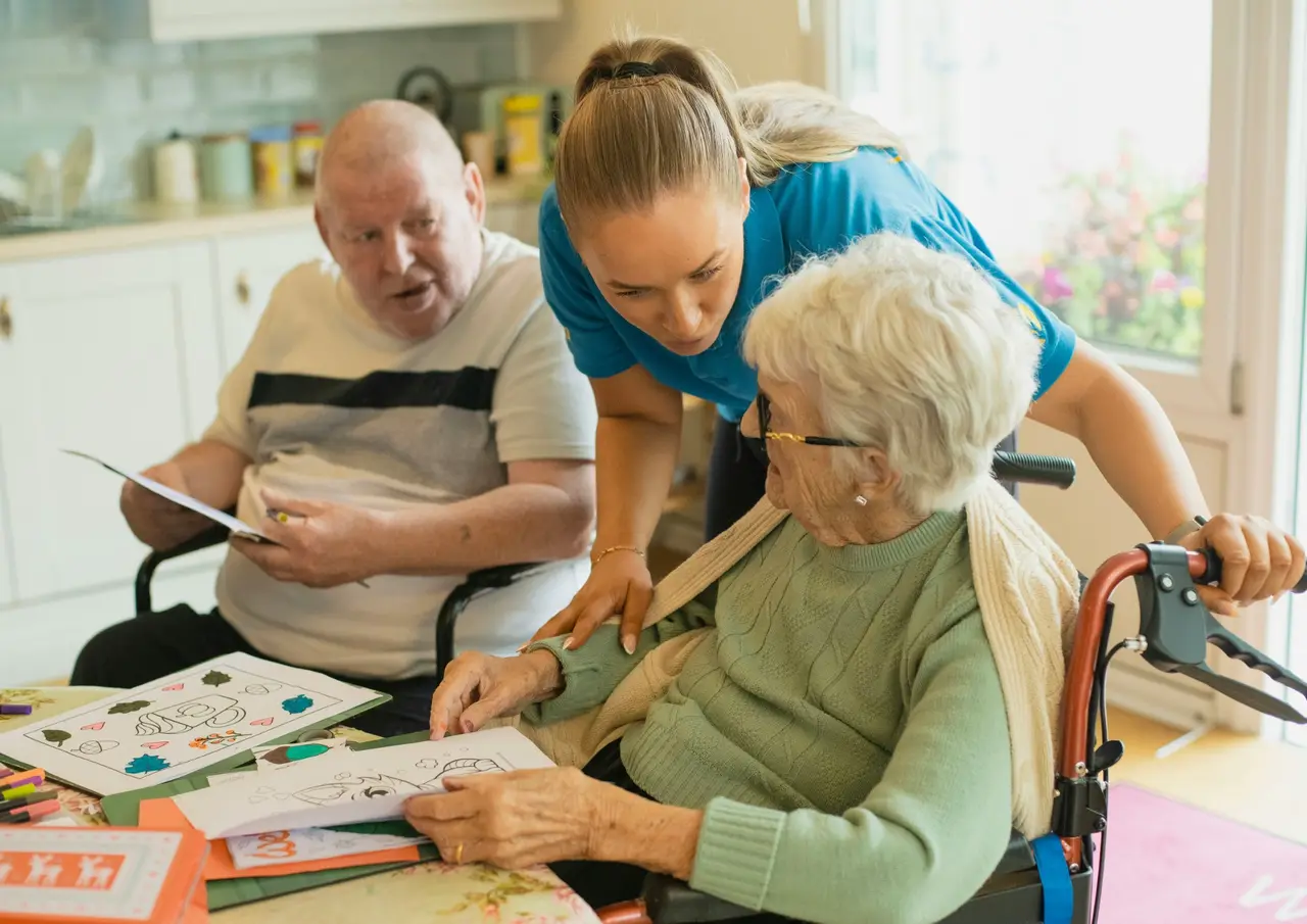 A carer helping two older adults with an activity at a kitchen table