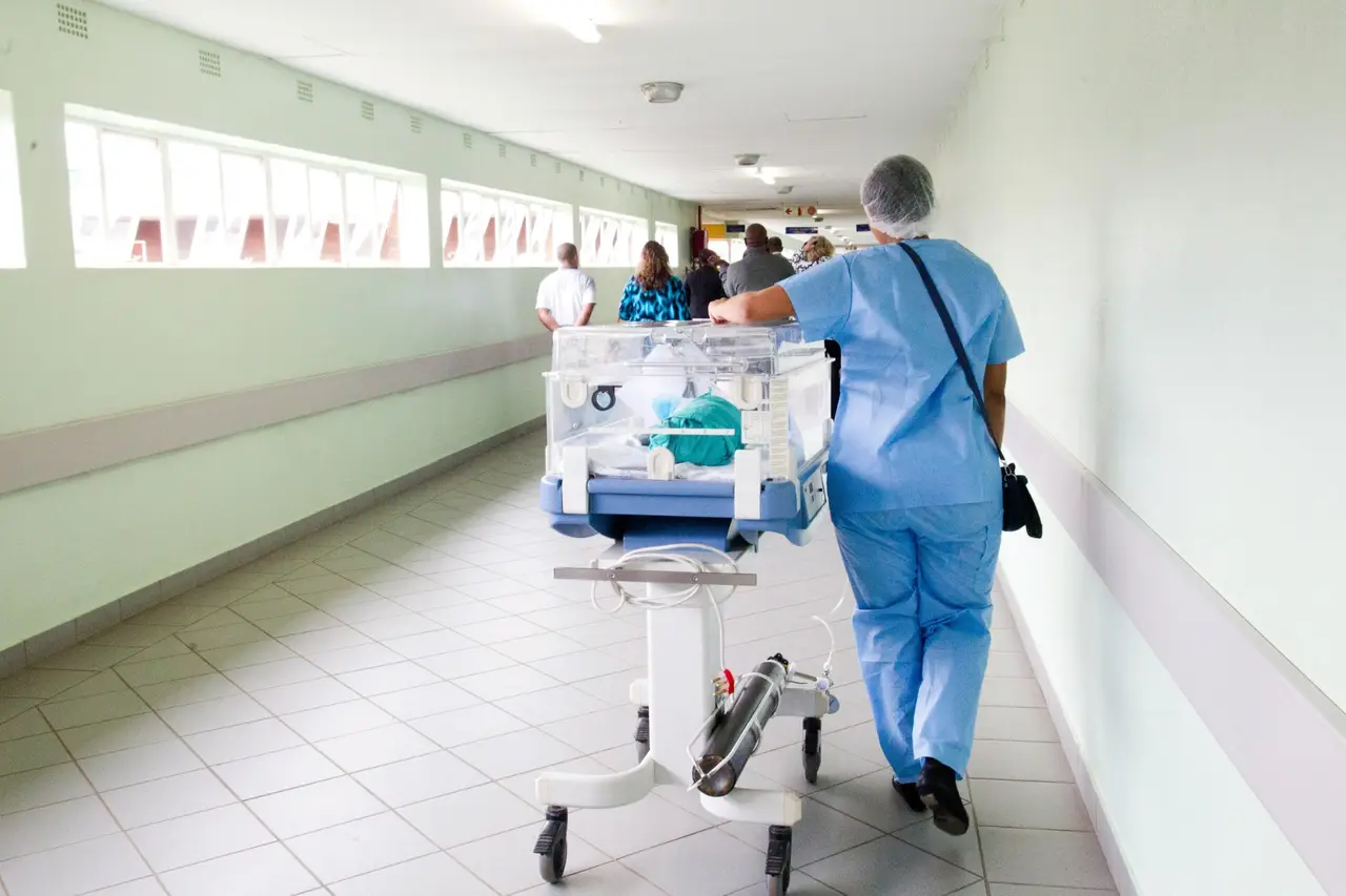 A nurse in scrubs moving equipment through a hospital corridor